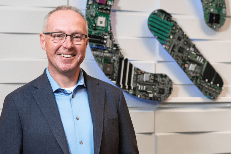 Teqworks President Matt Sidman standing in front of an art piece hanging in his office, the Teqworks Q made from circuit boards.